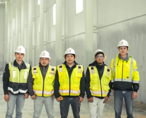 Equipo de trabajo con casco y chaleco reflejante posando dentro de nave industrial en construcción